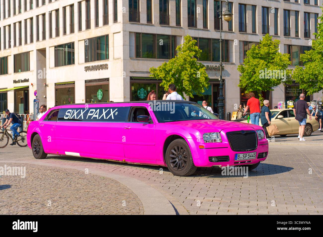 Berlin, Deutschland - 31. Mai 2025: Pulsierende rosa Limousine parkt am Pariser Platz, umgeben von moderner Architektur und Fußgängern, sonniger Tag, urbaner See Stockfoto