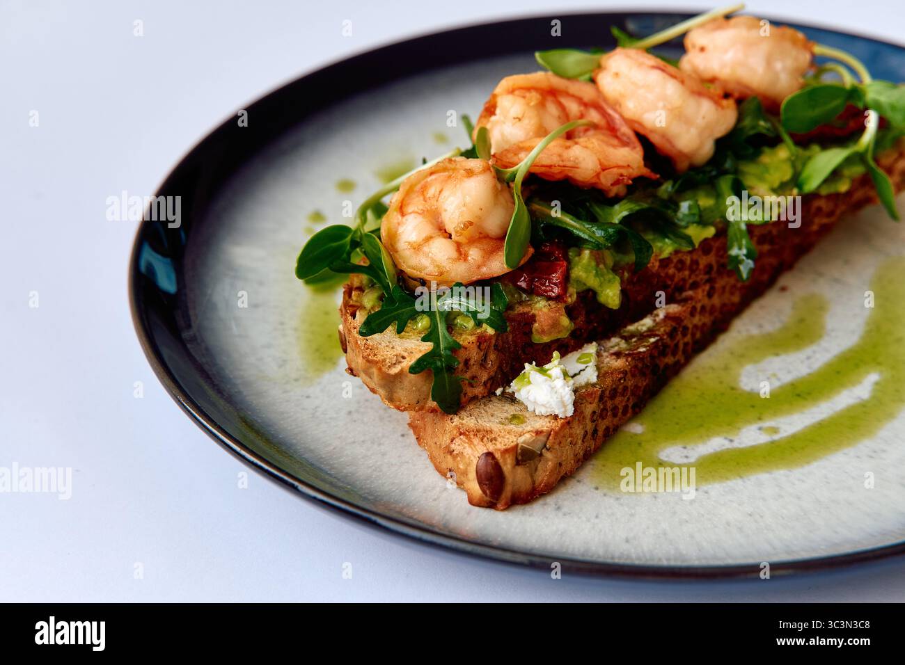 Köstlicher Shrimps-Toast mit frischem Gemüse und einem Hauch Olivenöl auf einer stilvollen schwarzen Platte Stockfoto