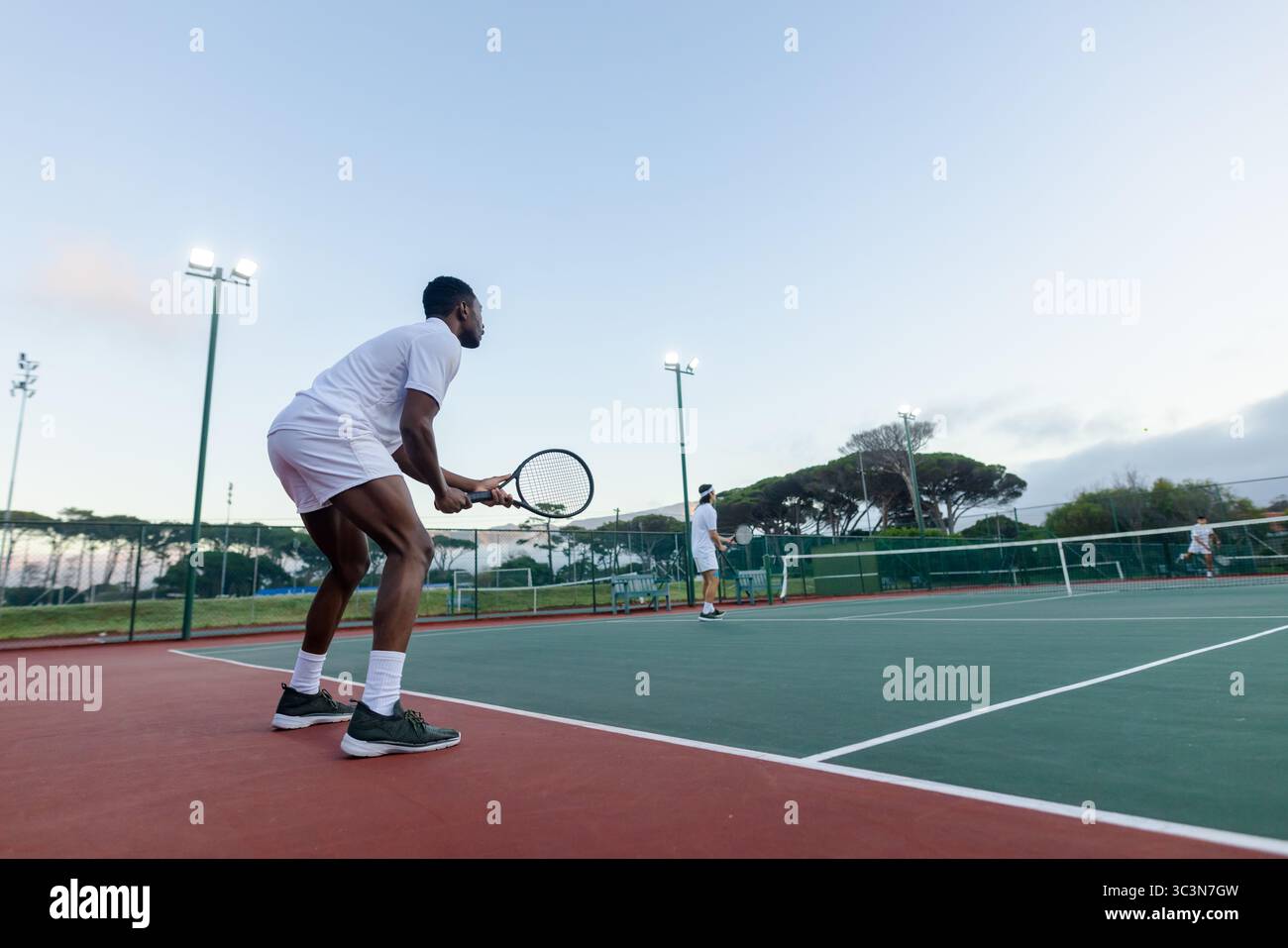 Männlicher afroamerikanischer Tennisspieler hält Schläger in der Nähe des Netzes in der Dämmerung, Kopierraum Stockfoto