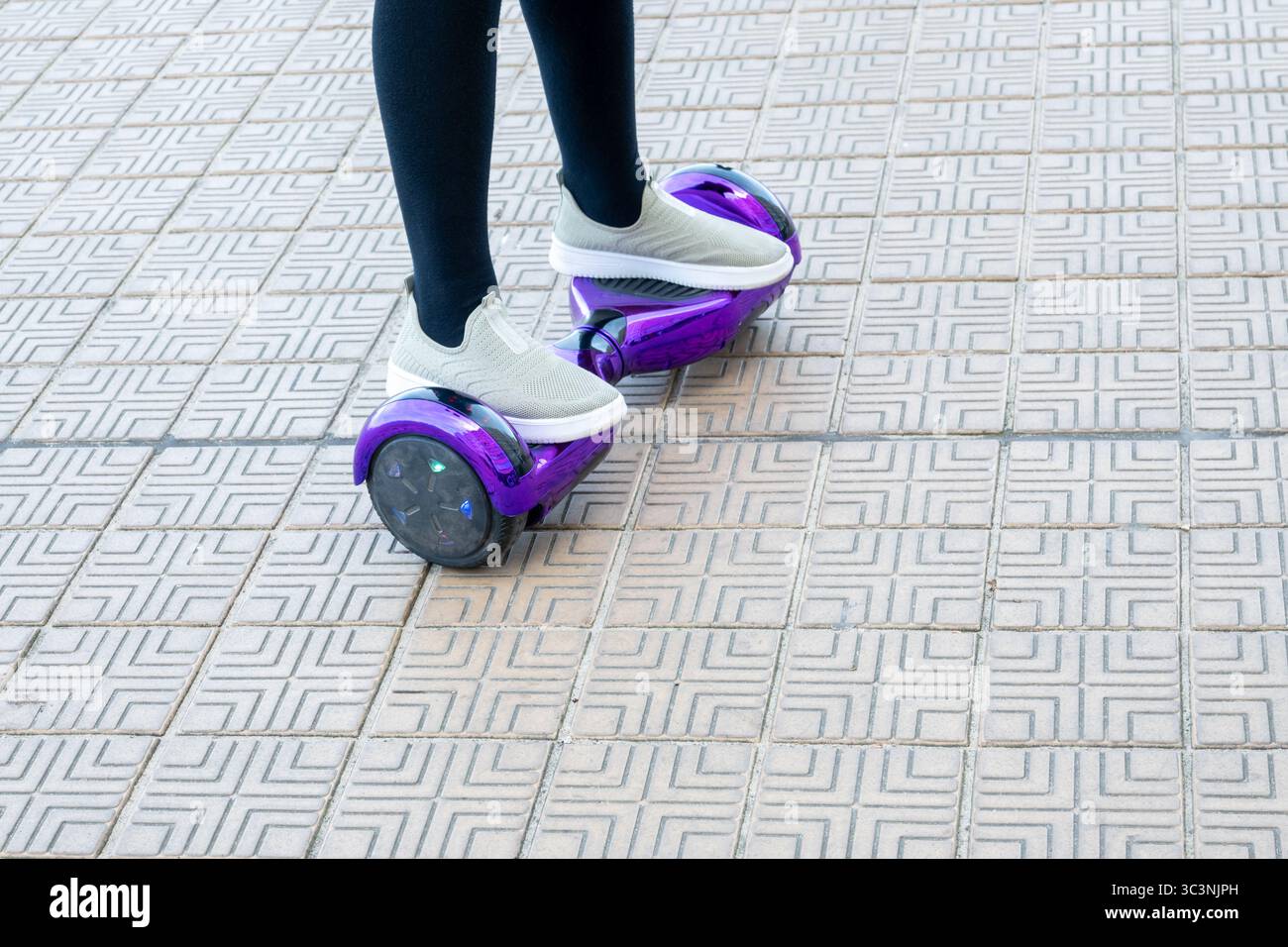 Mädchen in Turnschuhen, die auf dem Hoverboard auf der Backsteinstraße fahren. Neue Technologien. Selbstausbalancierendes elektrisches Smart Skateboard. Elektroroller für Spielspaß Stockfoto