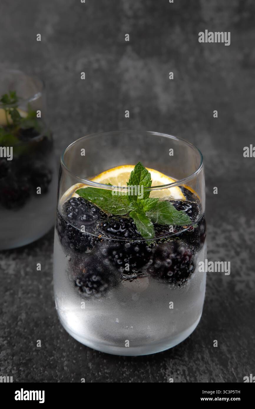 Zwei Gläser, mit schwarzem Hintergrund, mit einem erfrischenden Getränk aus Mineralwasser, Brombeeren, Zitrone, Minze Stockfoto