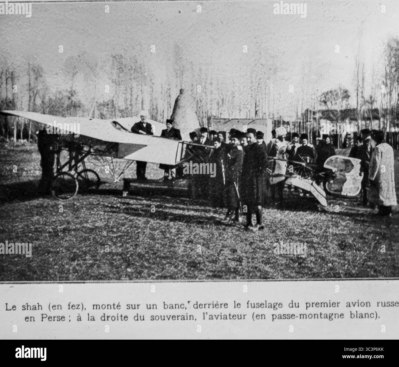 Der Schah von Persien, der hinter dem Rumpf des ersten russischen Flugzeugs im Iran sitzt, beobachtet das Flugzeug während einer Demonstration, begleitet von Würdenträgern und einem russischen Piloten in weißer Sturmhaube. Dieses Ereignis markiert die frühe russische Luftfahrt-Präsenz in Persien während der Kriegsdiplomatie und der technologischen Präsentation. Fotografiert um 1916. Veröffentlicht in L’Illustration, 18. März 1916. Stockfoto