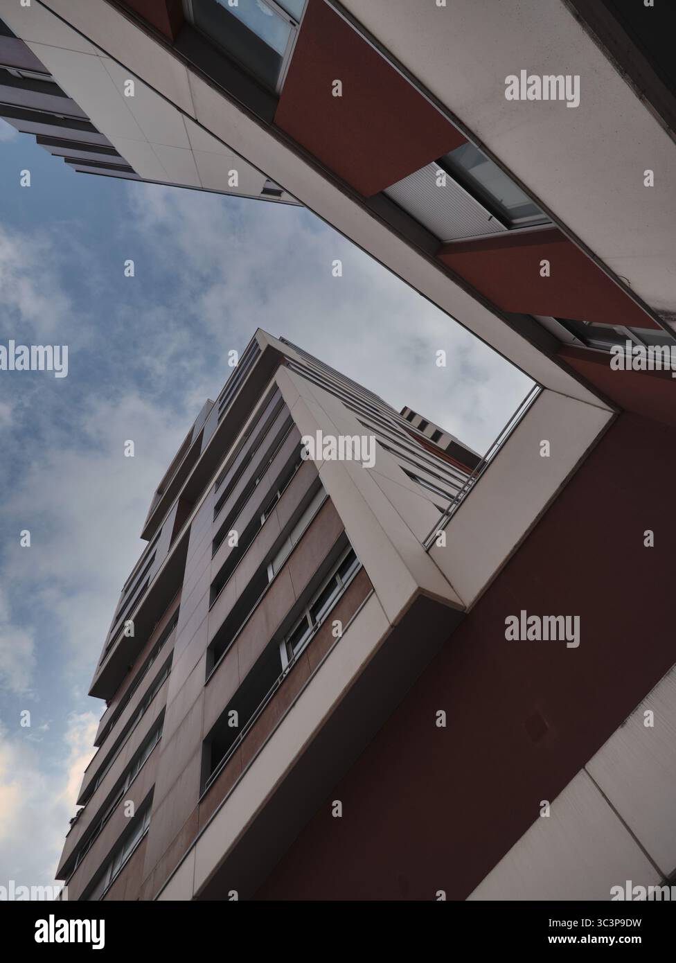 Blick nach oben auf ein modernes Gebäude mit eckigen architektonischen Merkmalen, großen Fenstern und roten Paneelen. Die Perspektive betont das HE Stockfoto