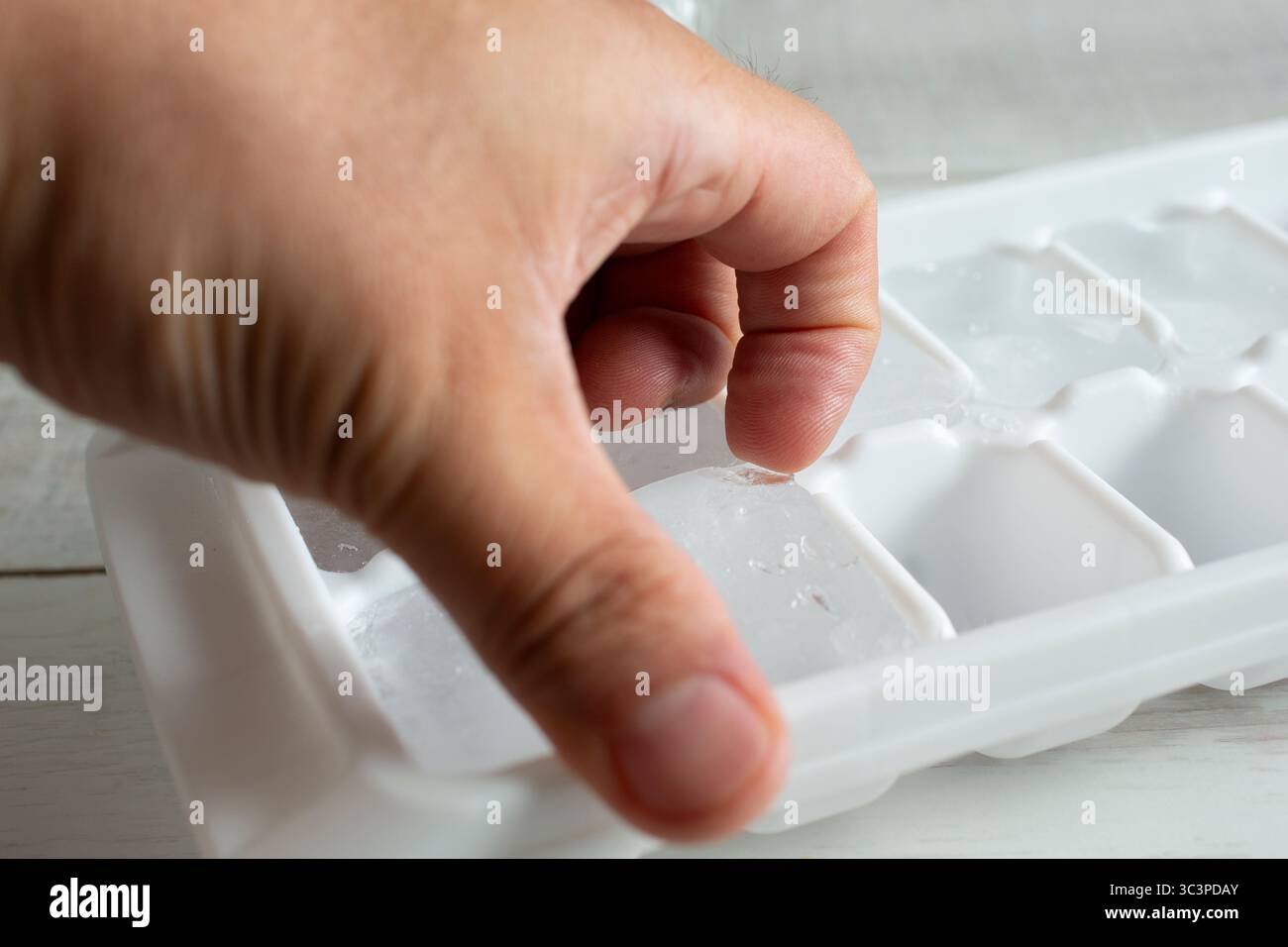Eine Nahaufnahme einer Hand, die einen Eiswürfel aus einem Tablett ausgräbt. Stockfoto