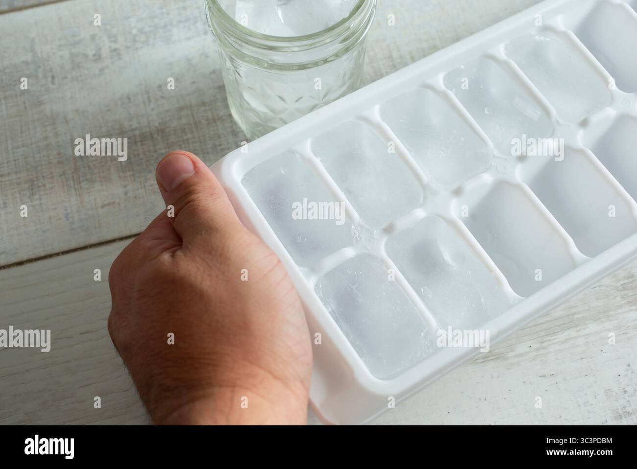 Eine Hand, die einen Eiswürfelbehälter vorbereitet. Stockfoto