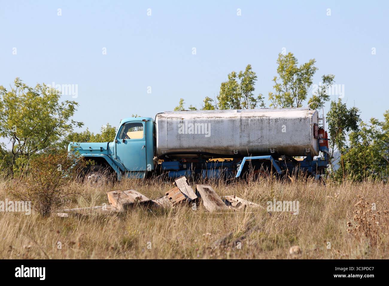 Ein verblasster blauer Wassertankwagen steht ungenutzt auf einem bewachsenen Grasfeld mit Rost- und Wetterflecken auf dem Metalltank und üppigem Grün Stockfoto