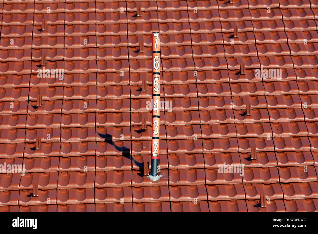 Ein mit Zahlen gekennzeichneter senkrechter Stab steht inmitten sauberer, roter Terrakotta-Dachziegel, der wahrscheinlich als Schneetiefe oder meteorologische Messung dient Stockfoto
