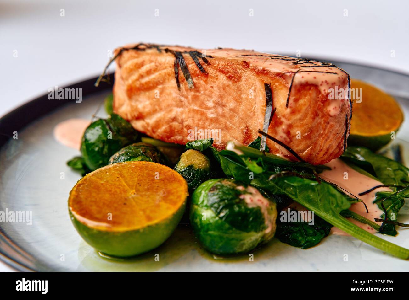 Köstlich gegrilltes Lachsfilet mit frischem Rosenkohl und Limettenscheiben, garniert mit einer cremigen Sauce für einen einladenden kulinarischen Genuss Stockfoto