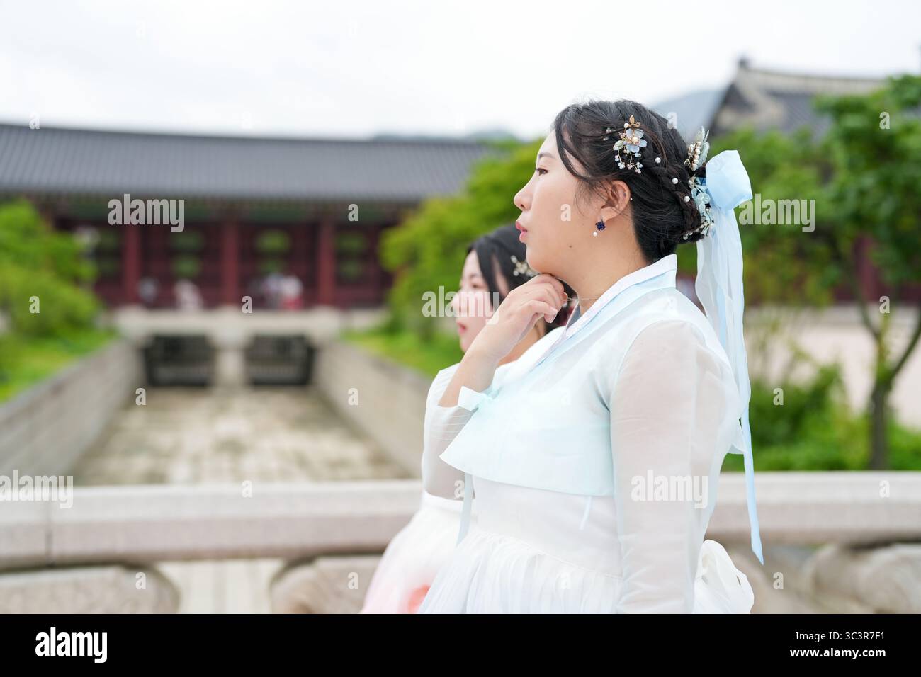 Zwei koreanische Frauen in ihren Zwanzigern gehen einfach über eine Steinbrücke im Gyeongbokgung Palace, tragen einen niedlichen rosa und himmelblauen Hanbok unter einem klaren Summ Stockfoto