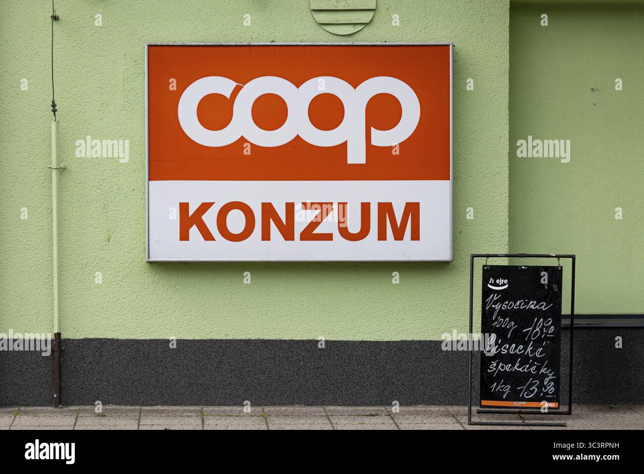 Großes COOP-Schild an einer grünen Wand neben einem kleinen Ladenfenster an der Kasse, ceska Kubice, Okres Domaslice, Tschechische Republik Stockfoto