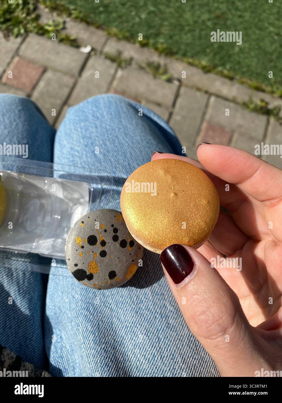 Zwei gemalte Steine in der Hand im Freien mit Sonnenlicht, einer aus Gold, einer aus Grau mit schwarzen Flecken. Mobiles Foto Stockfoto