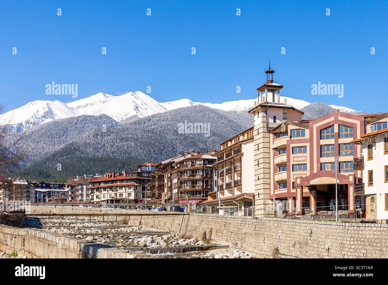 Bansko, Bulgarien - 9. April 2025: Fluss Glazne in bulgarischer Stadt, Hotelhäuser und schneebedeckte Gipfel des Pirin Stockfoto