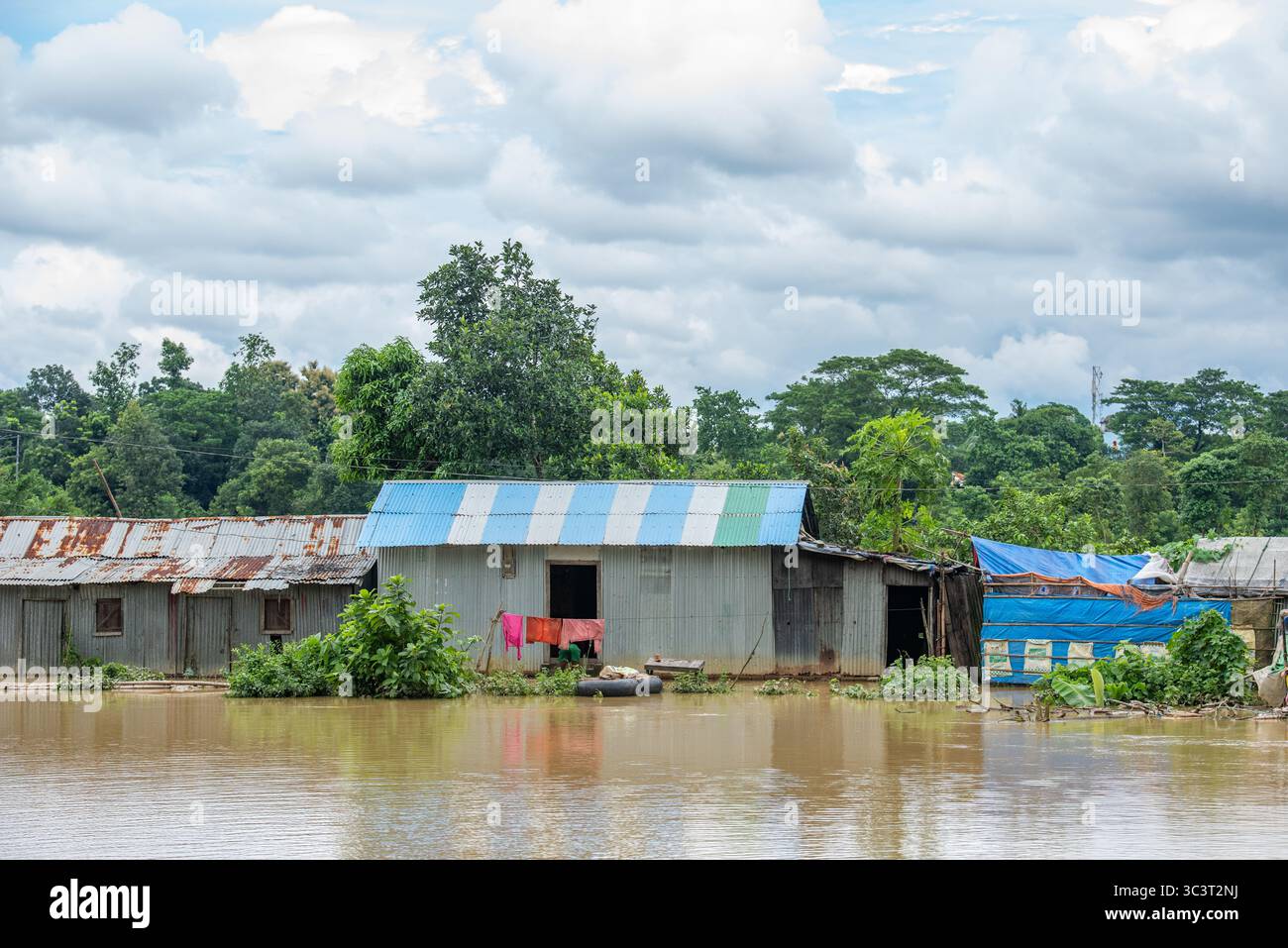 Überflutete Häuser in einer ländlichen Landschaft unter einem bewölkten Himmel. Überschwemmungen in Bangladesch sind eine immer wiederkehrende Naturkatastrophe, die vor allem auf seine geografische Lage zurückzuführen ist Stockfoto