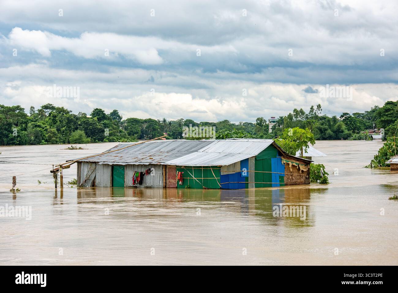 Überflutete Häuser in einer ländlichen Landschaft unter einem bewölkten Himmel. Überschwemmungen in Bangladesch sind eine immer wiederkehrende Naturkatastrophe, die vor allem auf seine geografische Lage zurückzuführen ist Stockfoto