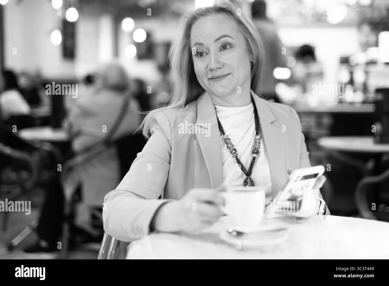 Frau sitzt am Tisch im Restaurant, trinkt Kaffee und schreibt eine Nachricht am Telefon. Stockfoto