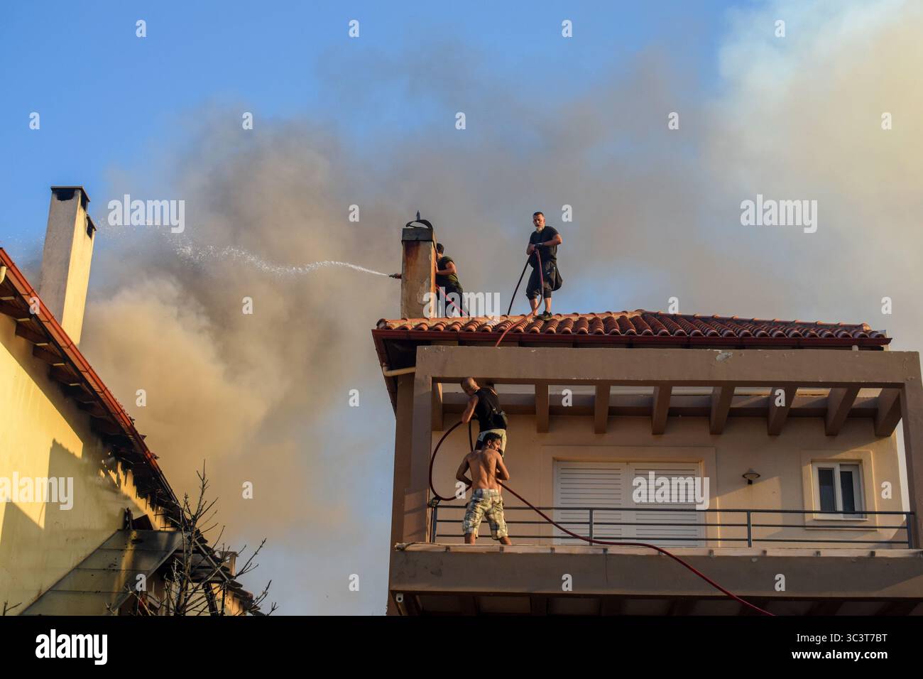 Athen, Griechenland, 26. Juli 2025. Freiwillige bekämpfen ein Feuer, das ein Haus verbrennt, während dicker Rauch aus dem Dach kommt. Ein wütendes Waldfeuer verwüstet das Wohngebiet Kryoneri, ein nördlicher Vorort der griechischen Hauptstadt inmitten einer intensiven Hitzewelle. Quelle: Dimitris Aspiotis/Alamy Live News Stockfoto