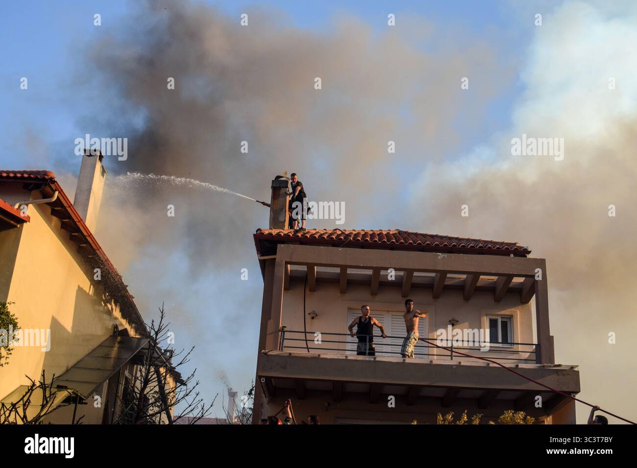 Athen, Griechenland, 26. Juli 2025. Freiwillige bekämpfen ein Feuer, das ein Haus verbrennt, während dicker Rauch aus dem Dach kommt. Ein wütendes Waldfeuer verwüstet das Wohngebiet Kryoneri, ein nördlicher Vorort der griechischen Hauptstadt inmitten einer intensiven Hitzewelle. Quelle: Dimitris Aspiotis/Alamy Live News Stockfoto