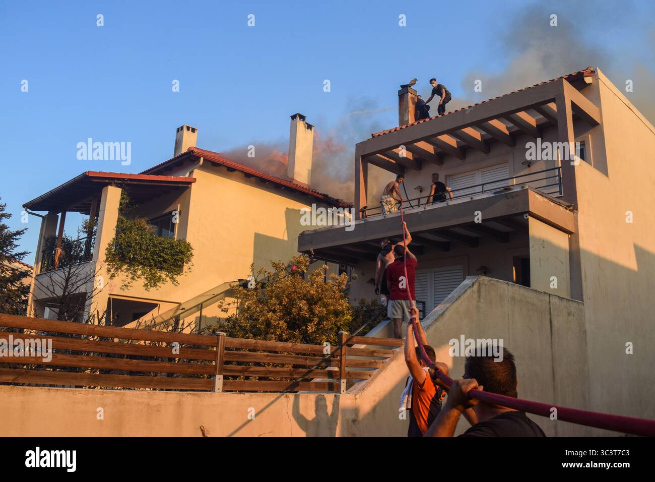 Athen, Griechenland, 26. Juli 2025. Freiwillige bekämpfen ein Feuer, das ein Haus verbrennt, während dicker Rauch aus dem Dach kommt. Ein wütendes Waldfeuer verwüstet das Wohngebiet Kryoneri, ein nördlicher Vorort der griechischen Hauptstadt inmitten einer intensiven Hitzewelle. Quelle: Dimitris Aspiotis/Alamy Live News Stockfoto