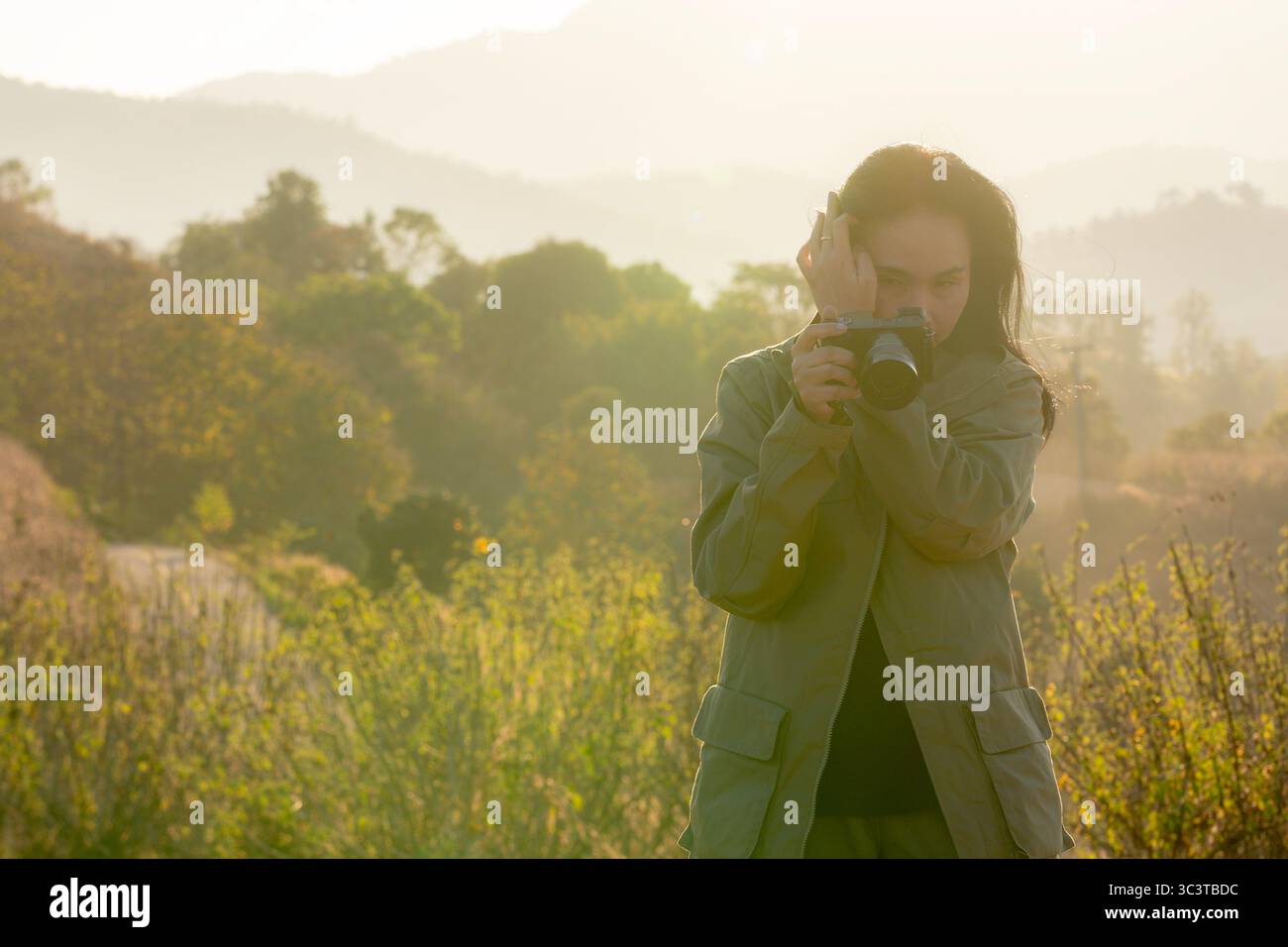 Eine Frau, die Fotos mit einer Digitalkamera in warmem goldenem Stundenlicht aufnimmt, umgeben von Natur und friedlicher Atmosphäre. Stockfoto