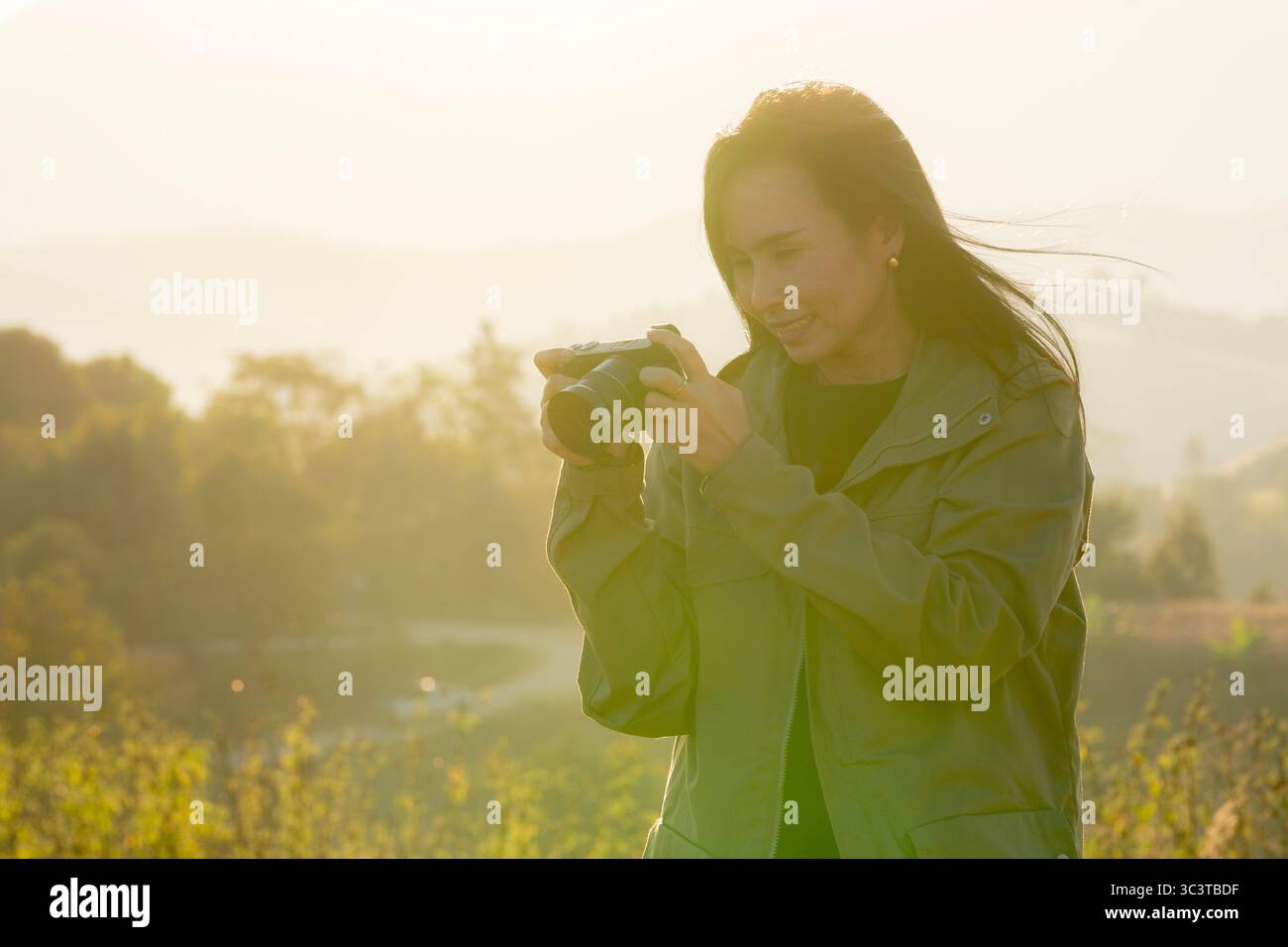 Eine Frau, die Fotos mit einer Digitalkamera in warmem goldenem Stundenlicht aufnimmt, umgeben von Natur und friedlicher Atmosphäre. Stockfoto