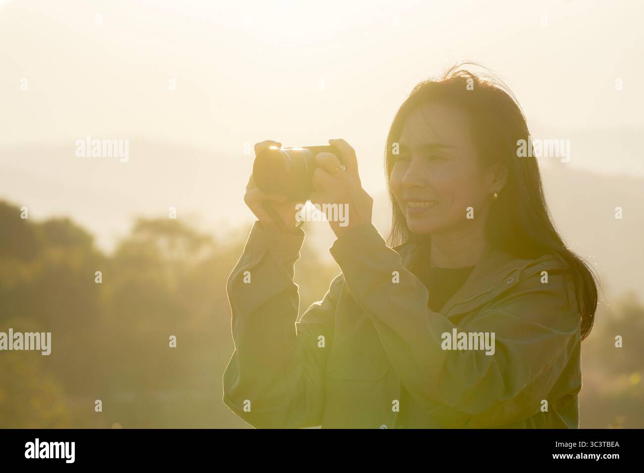 Eine Frau, die Fotos mit einer Digitalkamera in warmem goldenem Stundenlicht aufnimmt, umgeben von Natur und friedlicher Atmosphäre. Stockfoto