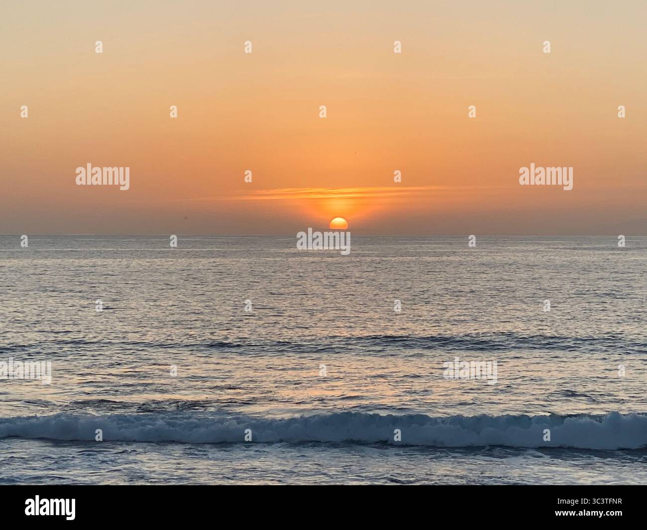 Ein atemberaubender Sonnenuntergang über dem Atlantischen Ozean, mit Wellen, die sanft zur Küste hin Rollen. Stockfoto