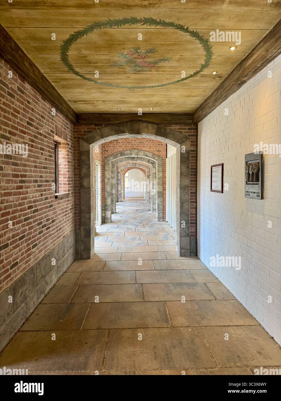 Eleganter, bogenförmiger Backsteinkorridor im Hansa Park, Deutschland, mit bemalter Decke und gemustertem Steinboden. Die symmetrischen Bögen und das Licht erzeugen einen - Smartphone-aufgenommenes Stockfoto