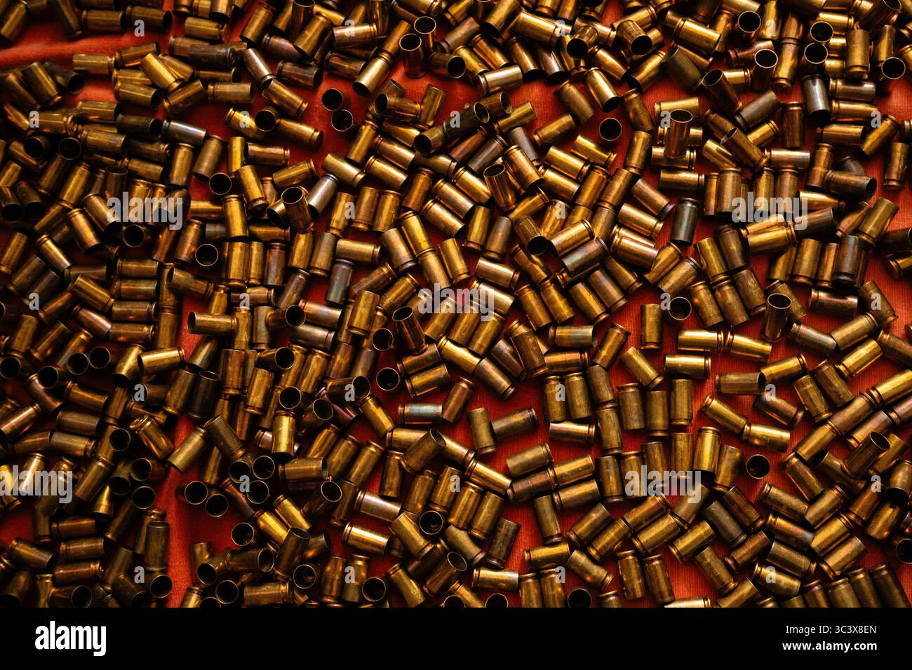 Gestreute Kupferkugelgehäuse auf rotem Hintergrund, die von warmem, metallischem Glanz erstrahlen und von warmem Licht beleuchtet werden Stockfoto