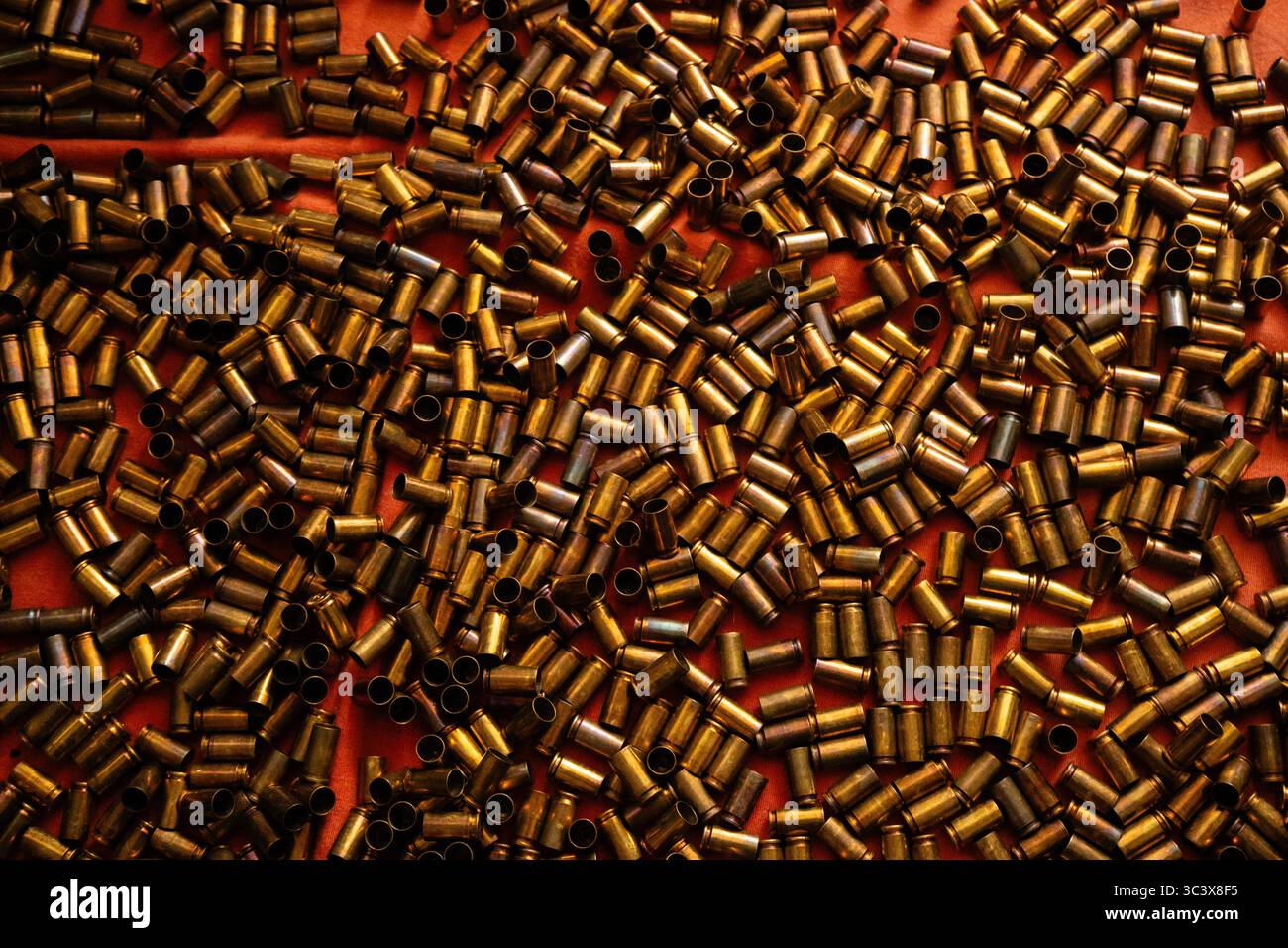 Gestreute Kupferkugelgehäuse auf rotem Hintergrund, die von warmem, metallischem Glanz erstrahlen und von warmem Licht beleuchtet werden Stockfoto