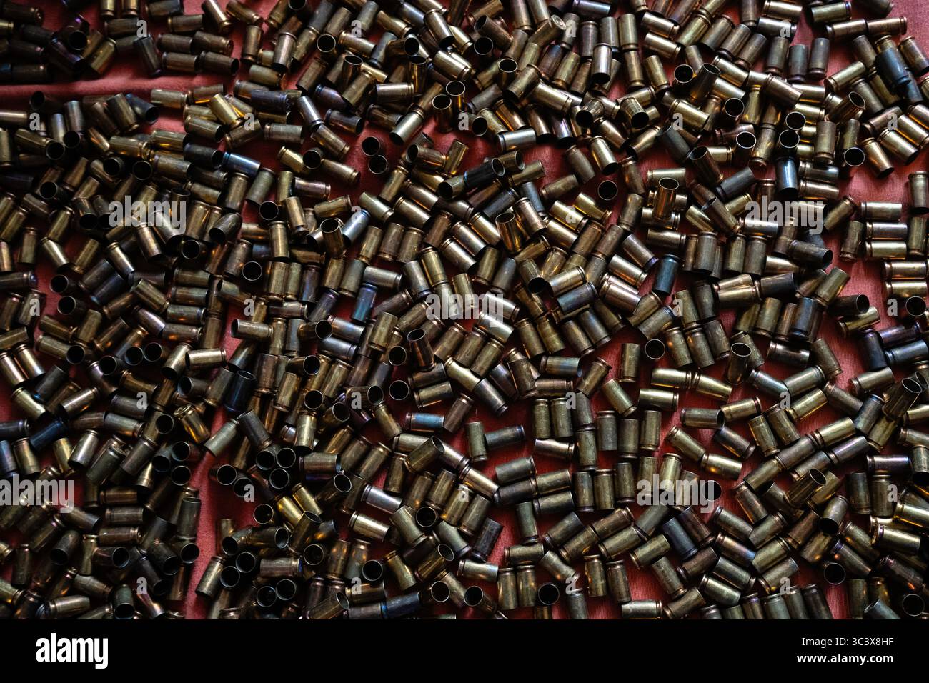 Verstreute Kupferkugelhüllen auf rotem Hintergrund, die von einem warmen metallischen Glanz glänzen, der von kaltem Licht beleuchtet wird Stockfoto