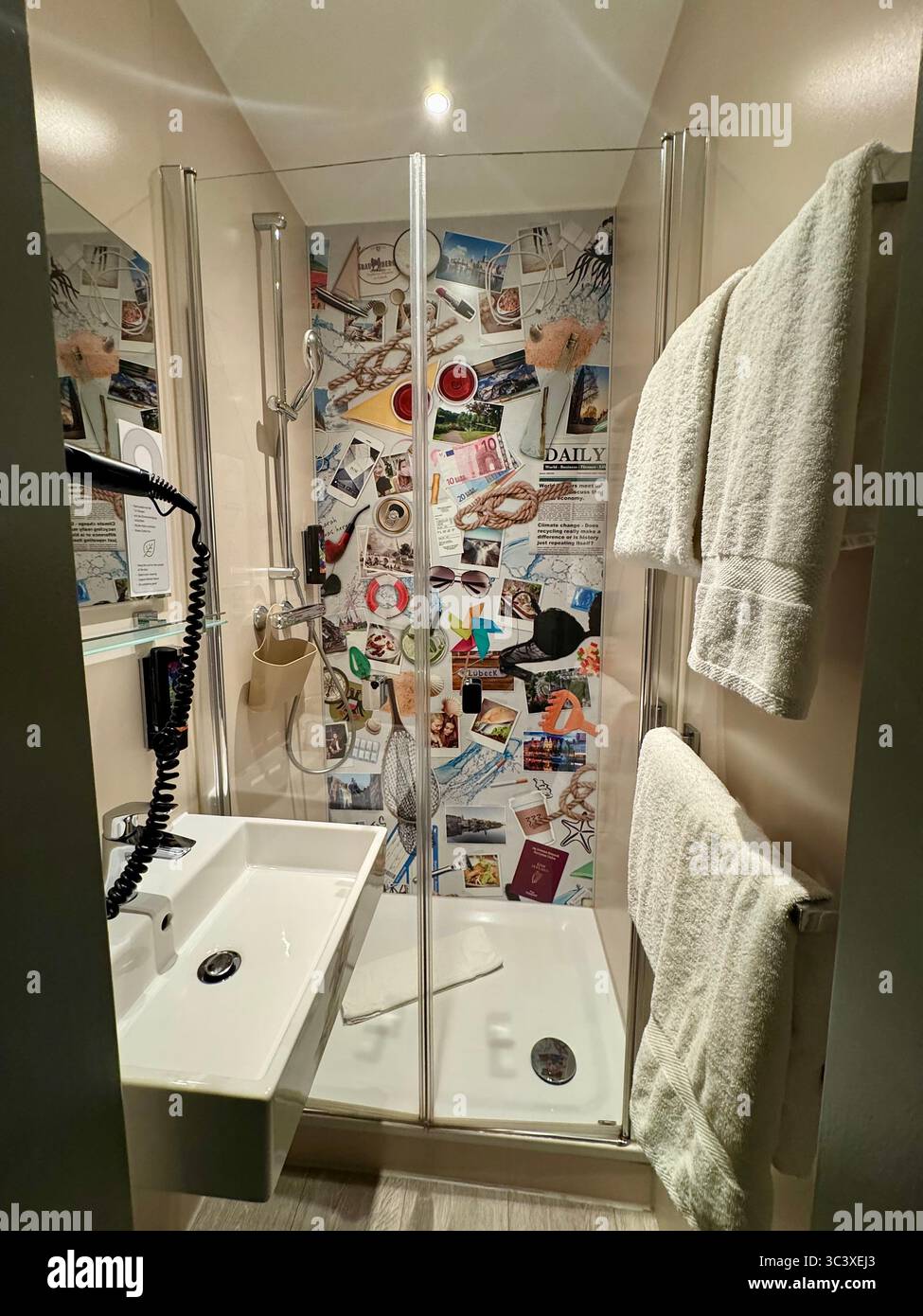 Modernes Hotelbad mit Glasdusche und dekorativer Wand im Stil einer Collage im NIU Hotel, Deutschland. - Smartphone-aufgenommenes Stockfoto