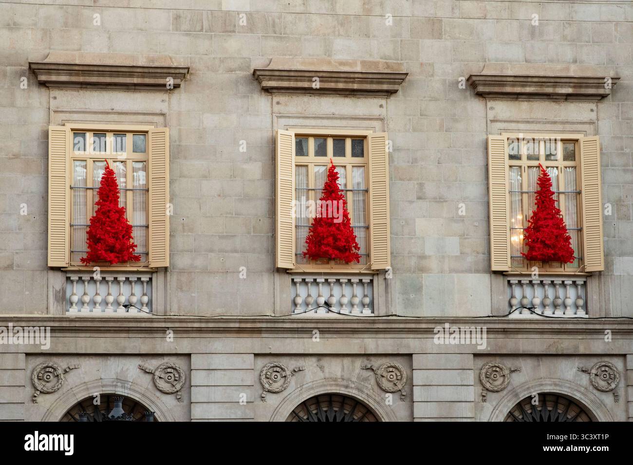 Leuchtend rote Weihnachtsbäume in den Fenstern historischer Häuser. Weihnachtsdekorationen, Ideen für die Dekoration der Fassade für das neue Jahr Stockfoto