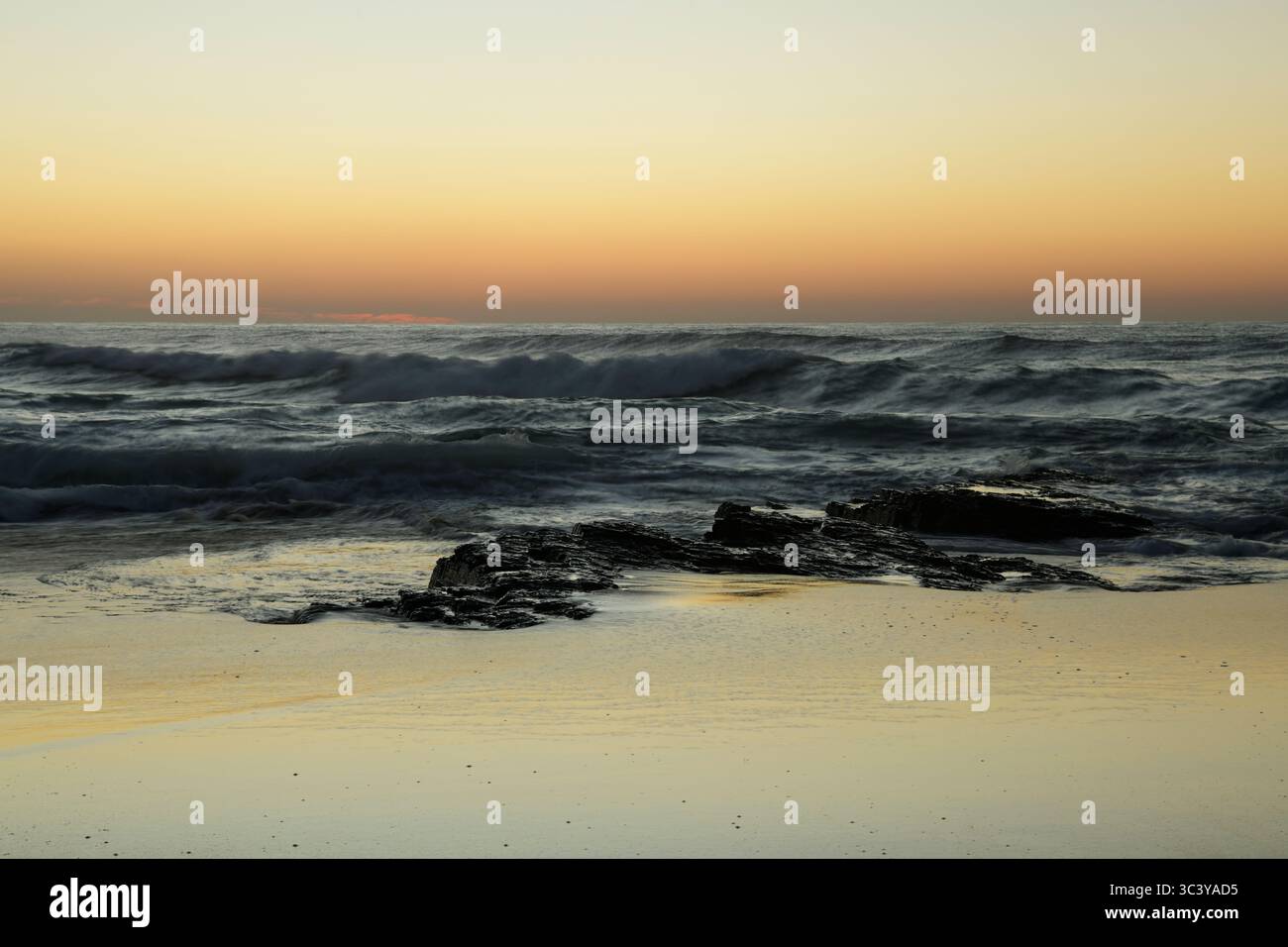 Wunderschöne Meereslandschaft mit brechendem Sonnenaufgang, stürzenden Wellen und goldenen Reflexen auf nassem Meersand, Winklespruit Beach, Amanzimtoti, Südafrika, Bewegungsunschärfe Stockfoto