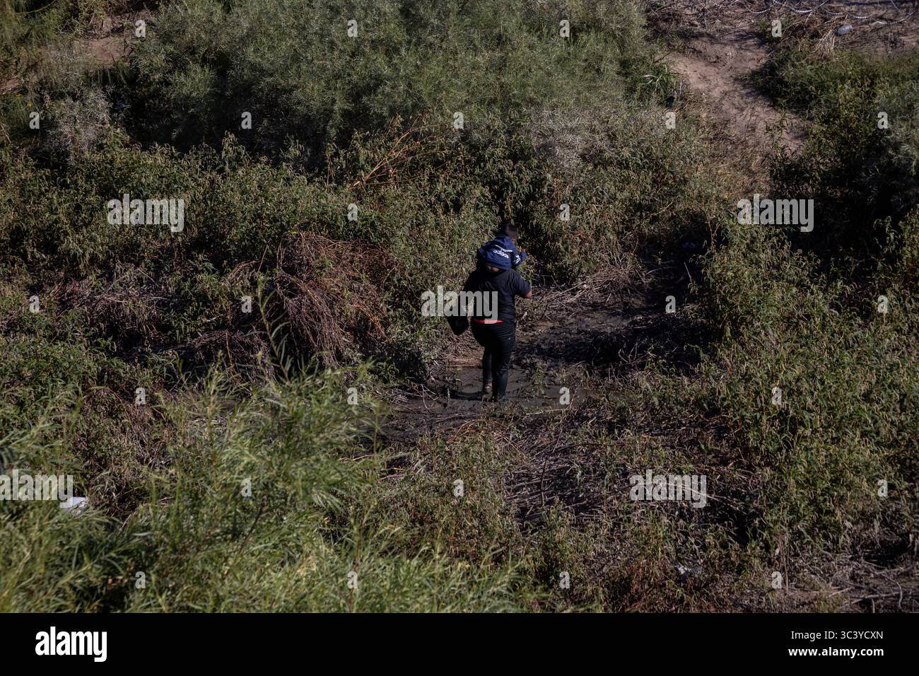 Individual durchquert schlammigen Pfad in der Nähe von Ciudad Juarez, Eimer in der Hand, inmitten von Migrationsproblemen. Stockfoto