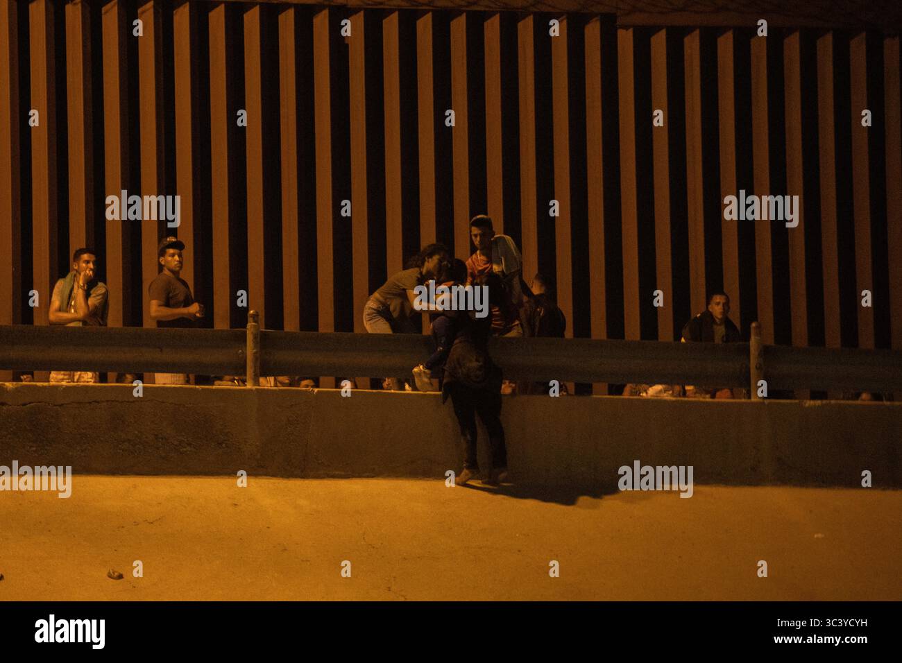 Migranten sammeln sich nachts an der Barriere in Ciudad Juarez, was die anhaltenden Migrationsherausforderungen widerspiegelt. Stockfoto