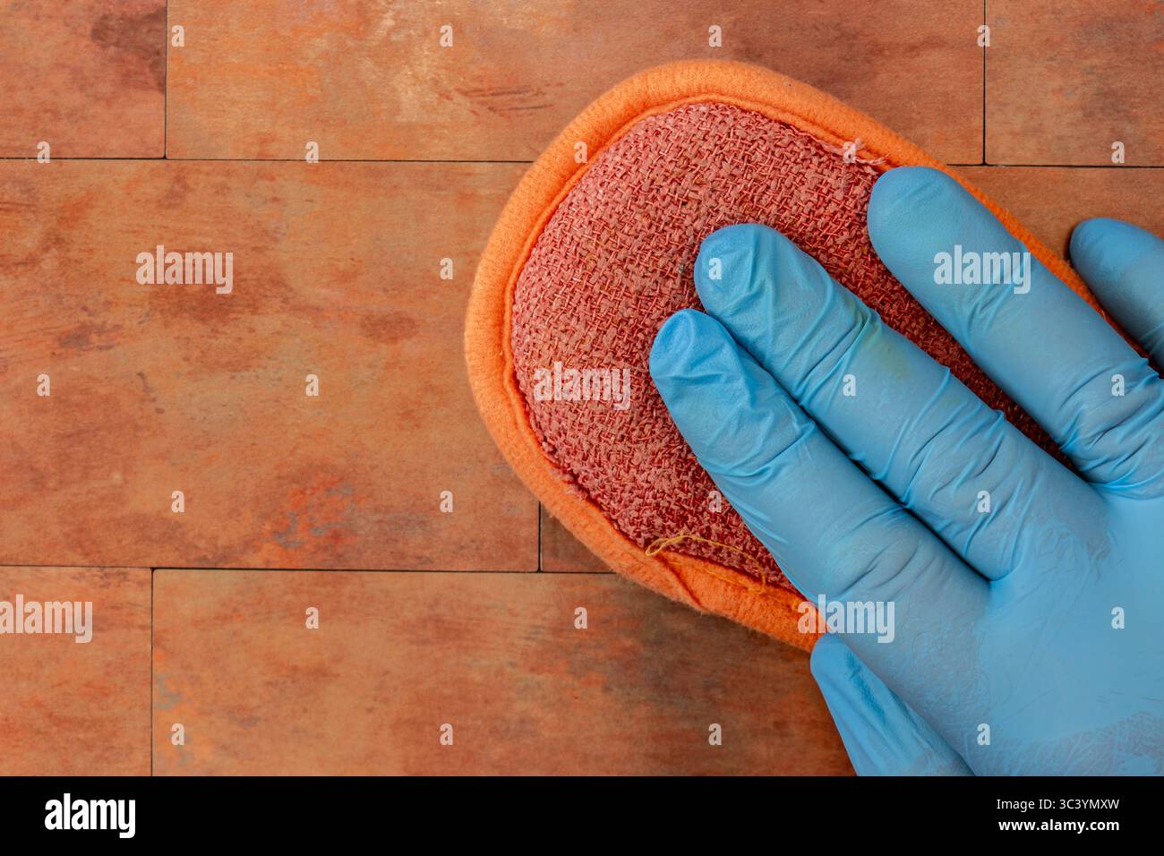 Person, die Gummihandschuhe trägt und mit einem scheuernden padl kupferne Fliesen reinigt. Hausarbeit-Chore-Konzept. Stockfoto
