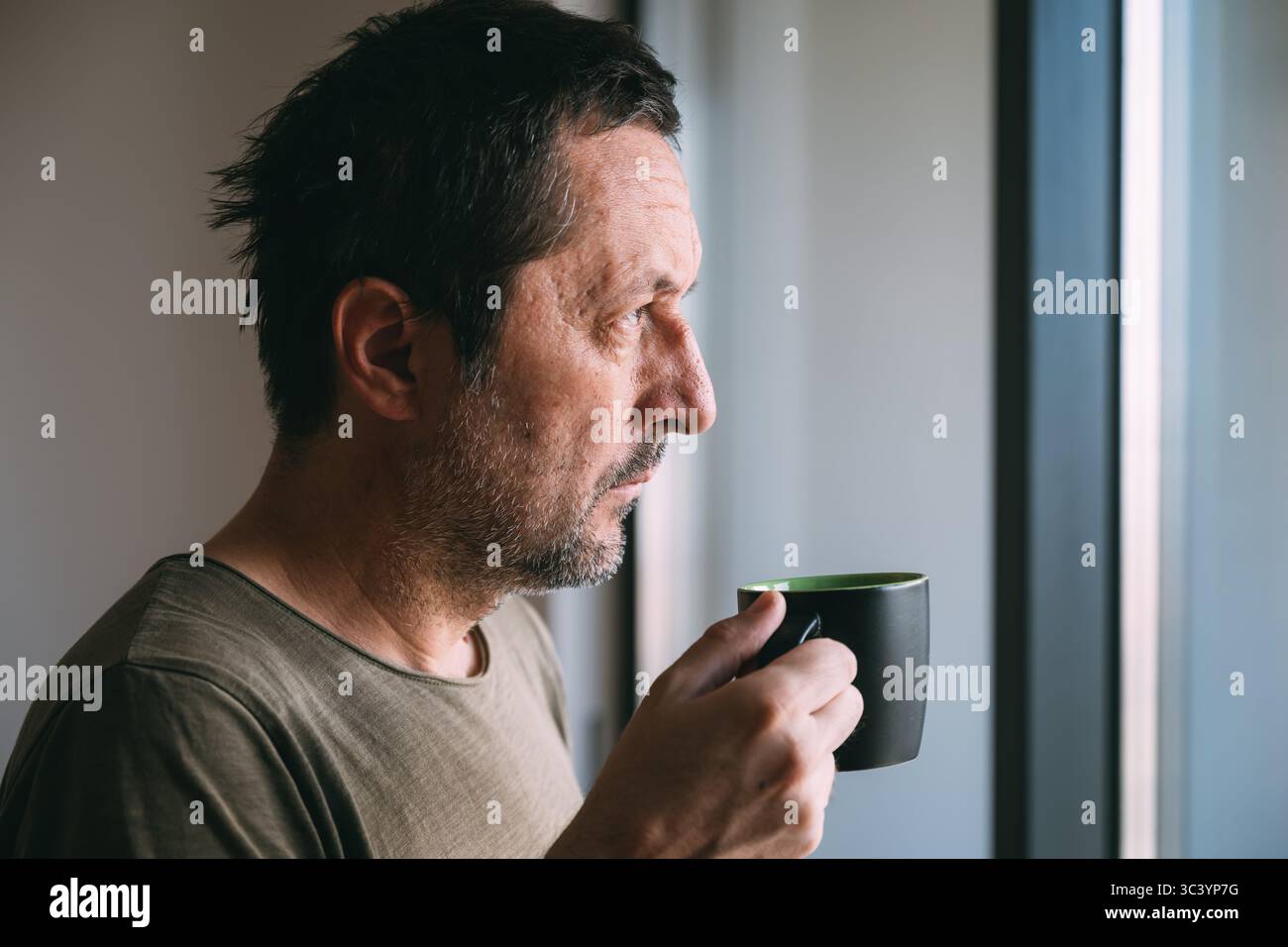 Trinken von heißem Tee oder Kaffee, während Sie hinausschauen und nachdenken, Porträt eines erwachsenen Mannes zu Hause, selektiver Fokus Stockfoto