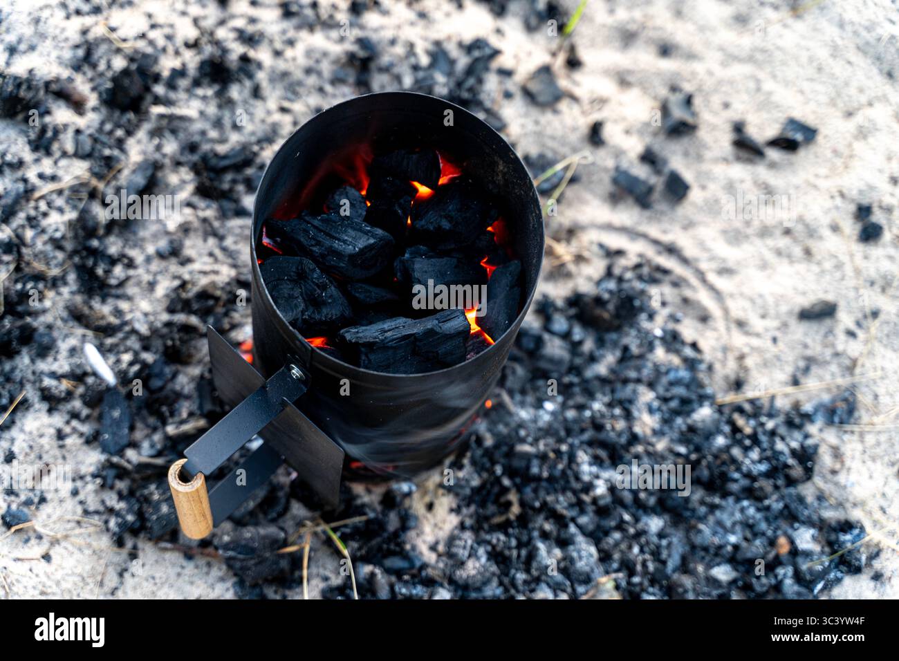 Nahaufnahme eines Holzkohlekamins mit glühenden Kohlen am Sandstrand - tragbares Feuerstartwerkzeug für umweltfreundliches Kochen im Freien Stockfoto