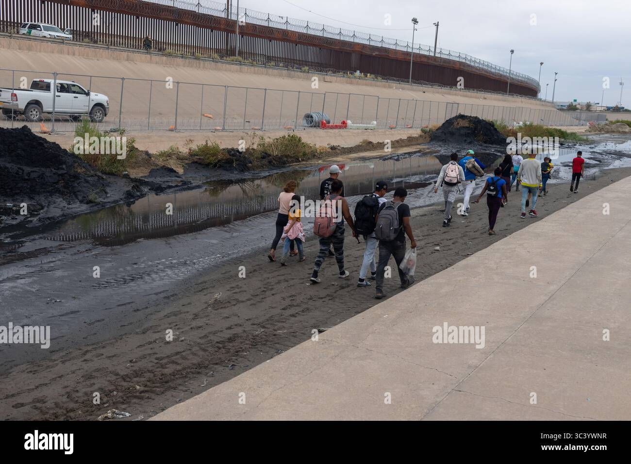 Gruppe von Migranten, die am Grenzzaun von Ciudad Juarez vorbeilaufen, spiegelt die anhaltenden Migrationsherausforderungen wider. Stockfoto