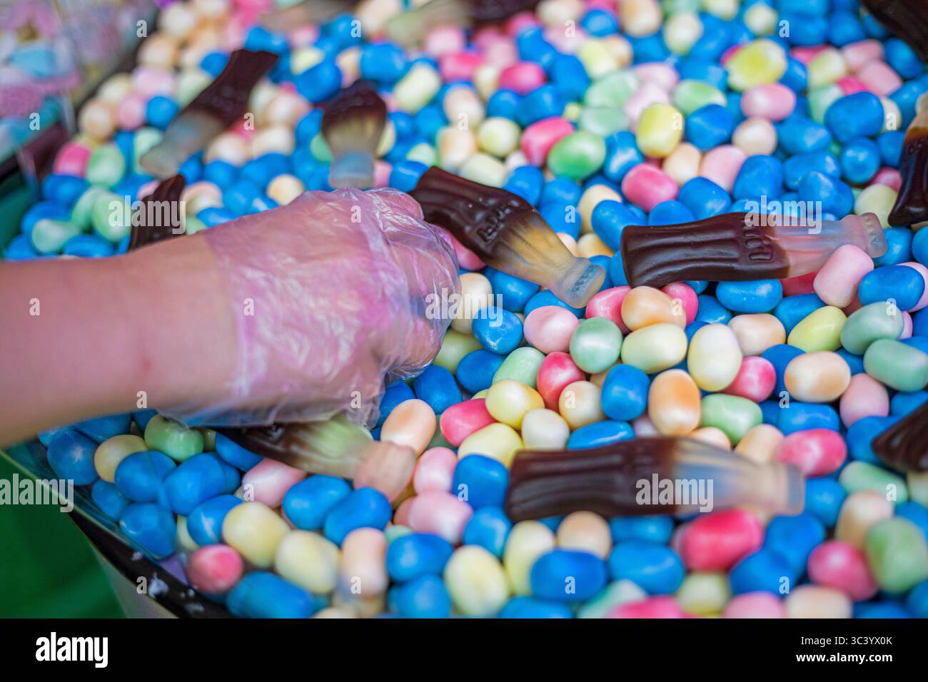 Nehmen Sie Gelee-Bonbons mit einer Hand in einem Einweghandschuh zum Kauf auf Stockfoto
