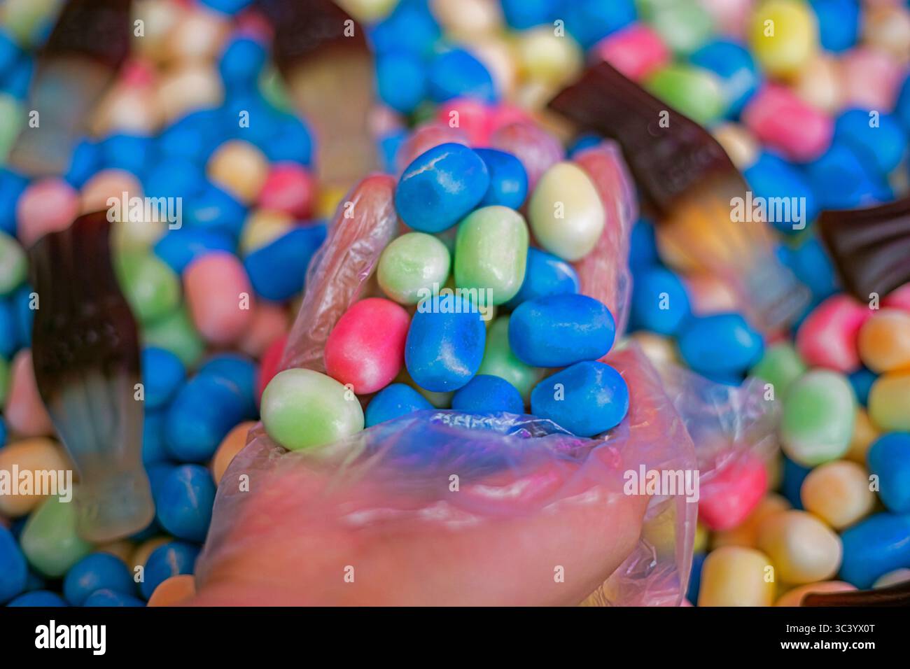 Nehmen Sie Gelee-Bonbons mit einer Hand in einem Einweghandschuh zum Kauf auf Stockfoto