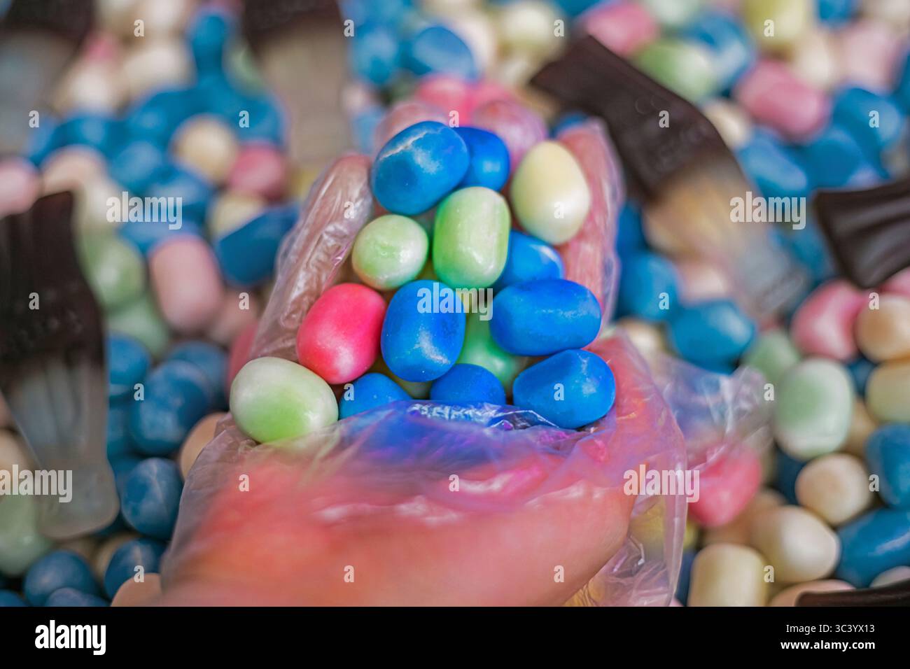 Nehmen Sie Gelee-Bonbons mit einer Hand in einem Einweghandschuh zum Kauf auf Stockfoto