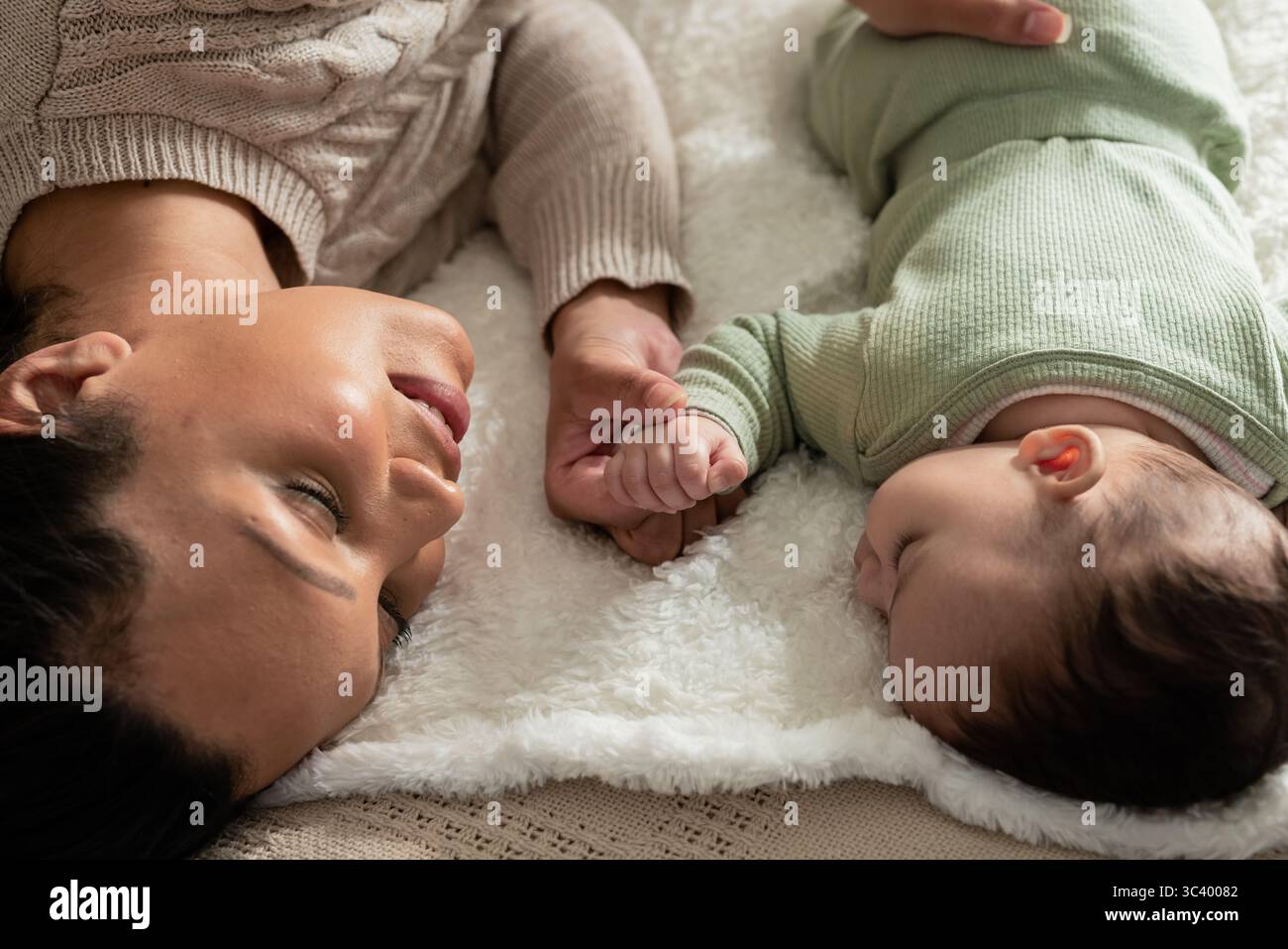 Mittelerwachsene Frau und Kleinkind, die auf weißer Plüschdecke liegen und Hände im Schlafzimmer halten Stockfoto