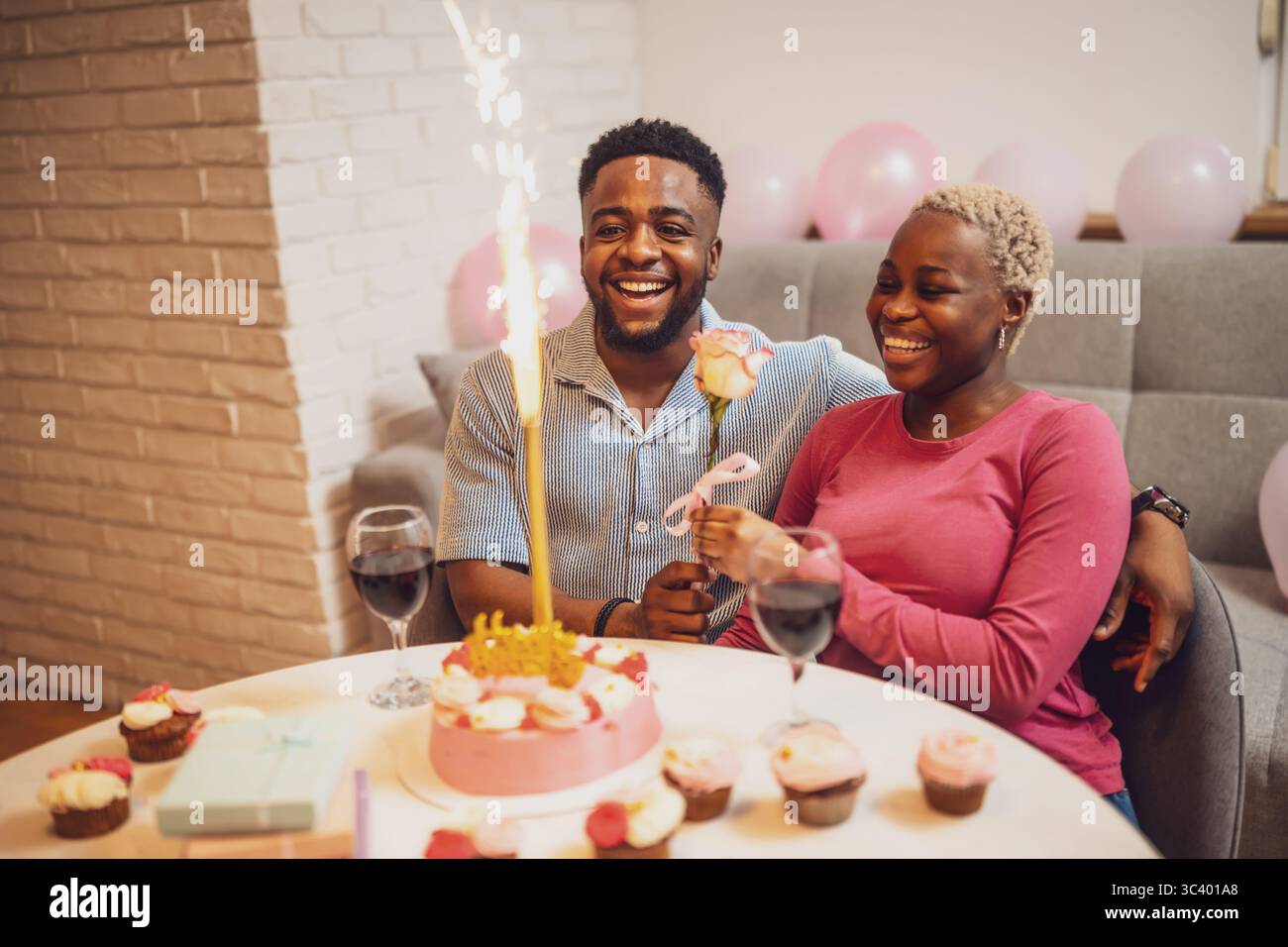 Glückliches junges Paar, das zu Hause den Geburtstag der Frau feiert. Sie sind glücklich und der Freund gibt seiner Freundin Rose. Stockfoto