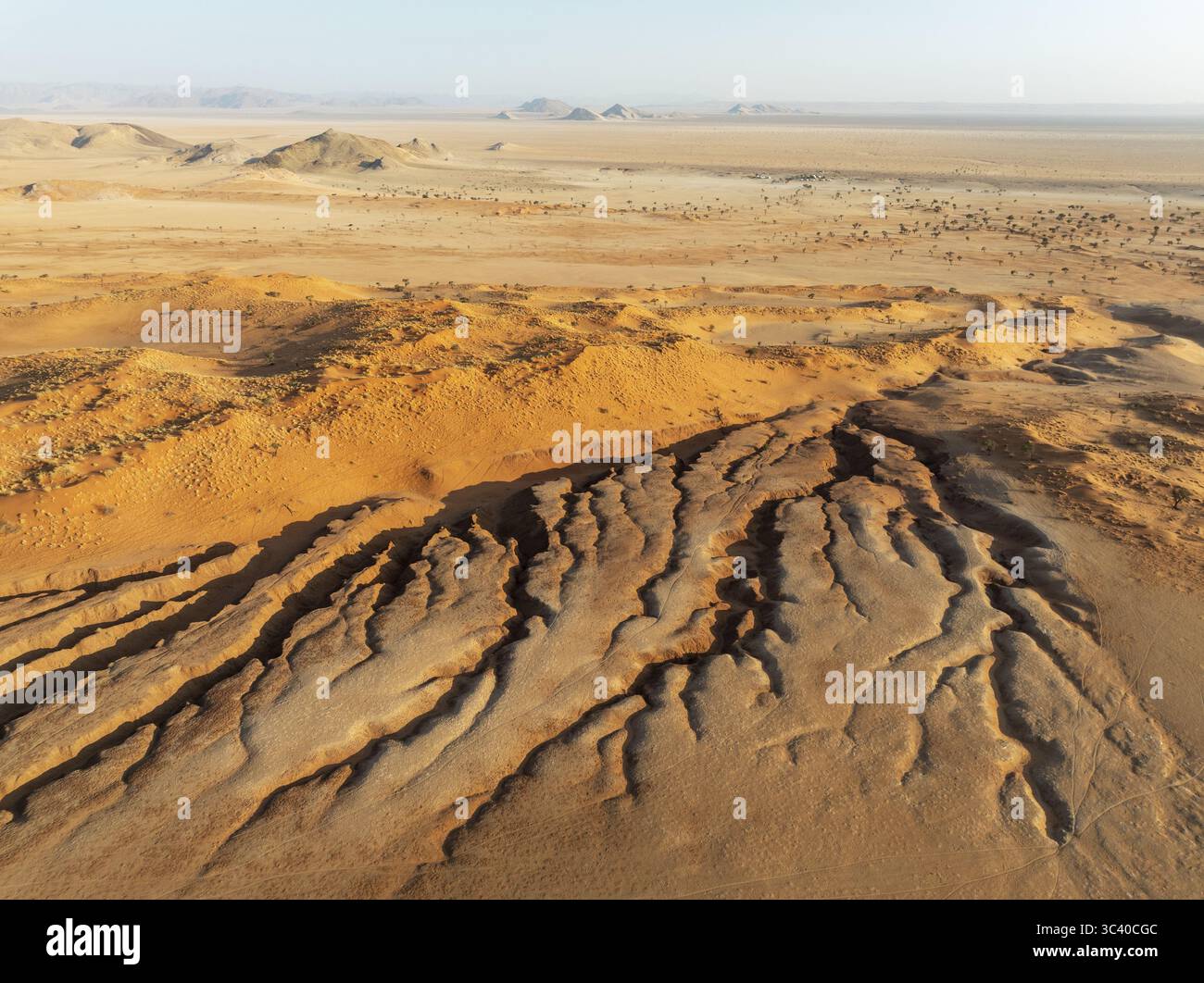 Aus der Vogelperspektive der trockenen Landschaft erschließt sich ein Wandteppich aus ockerfarbenen Dünen und rauer, skulpturaler Erde unter einem riesigen Himmel, Tsondab Valley, Khomas, Namibia. Stockfoto