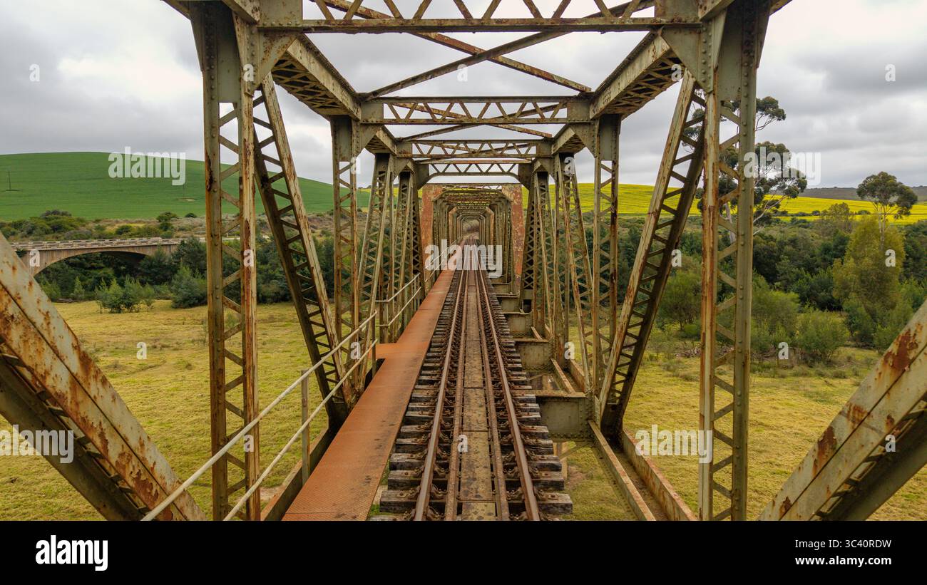 Aus der Vogelperspektive der verrosteten Eisenbahnbrücke, die sich in Richtung Goldfelder unter einem Himmel von brodelnden Wolken erstreckt, Riversdale, Westkap, Südafrika. Stockfoto