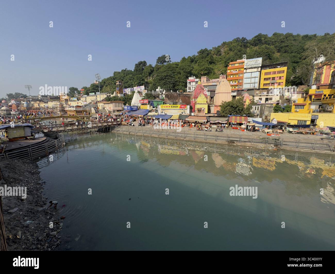 Fluss mit angrenzenden bunten Gebäuden, ruhiges Wasser, blauer Himmel, Har Ki Pauri, Ganges, Haridwar, Uttarakhand, Indien Stockfoto