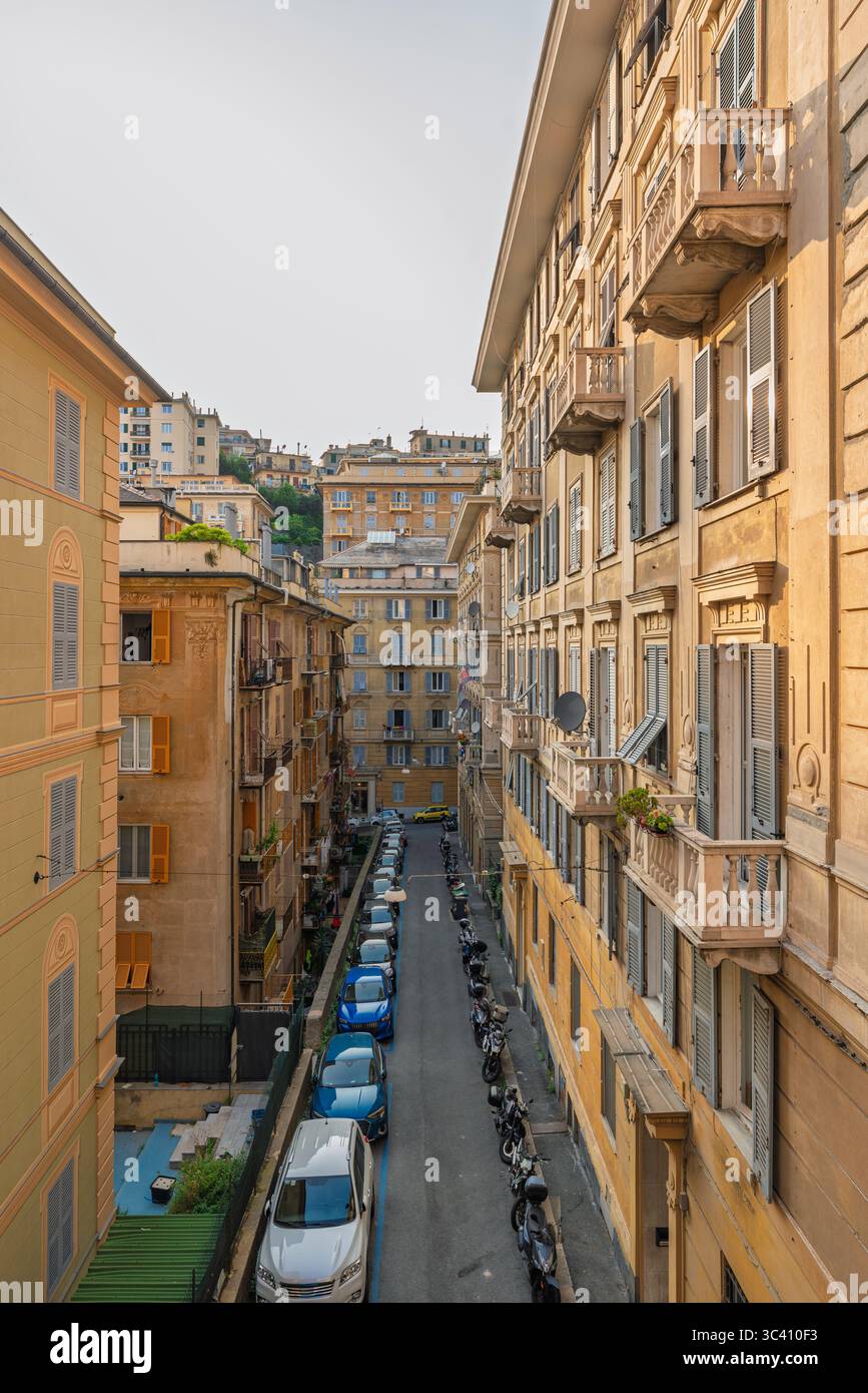 Das Sonnenlicht beleuchtet eine charmante, enge Straße in Genua, Italien, mit historischen Gebäuden und geparktem Fahrzeug Stockfoto