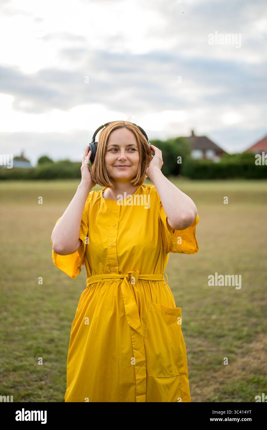 Eine fröhliche Frau mittleren Alters, die ein gelbes Kleid mit Kopfhörern trägt Stockfoto