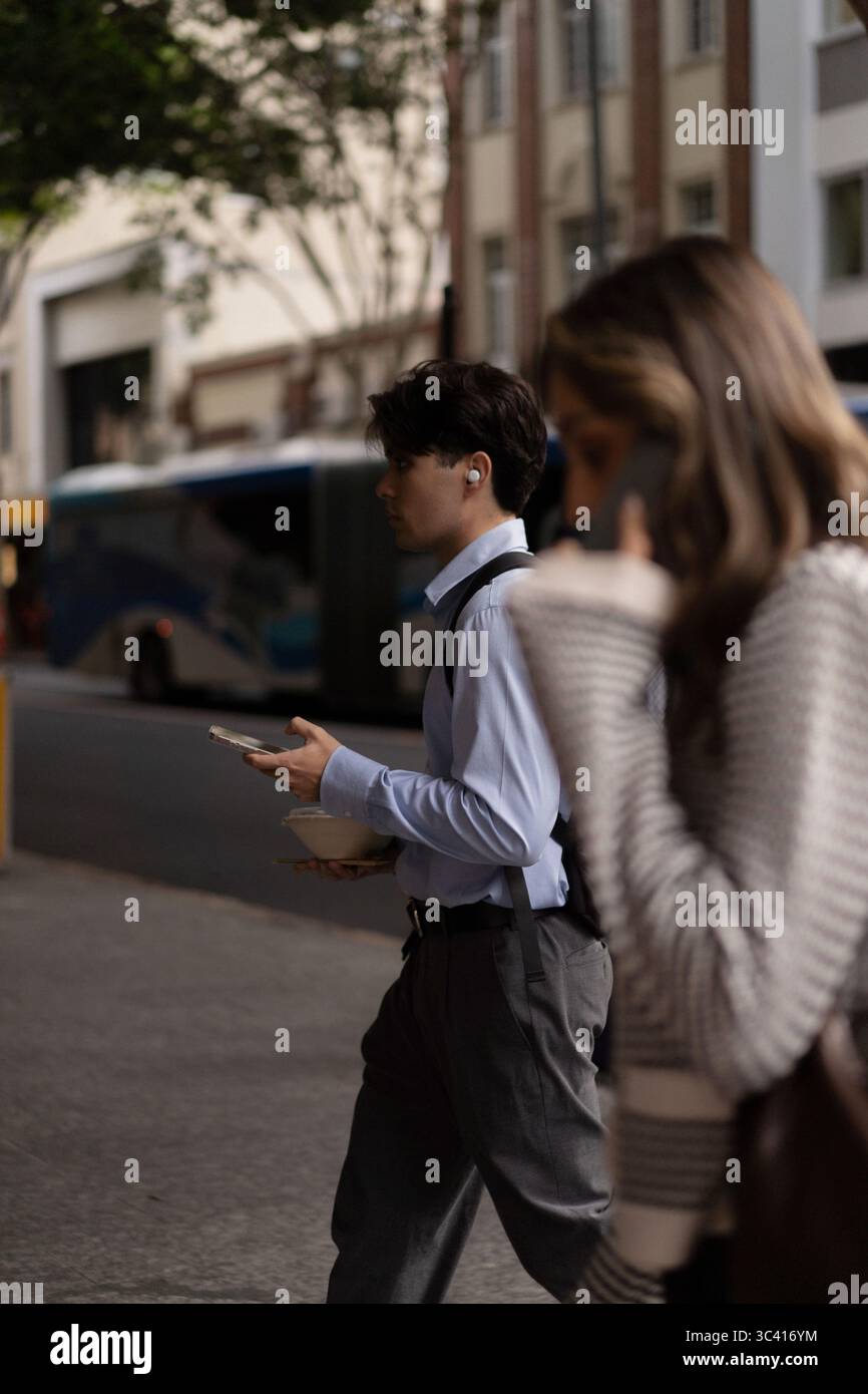Junger Mann, der mit Essen und schnurlosen Ohrstöpseln durch die Stadt geht Stockfoto